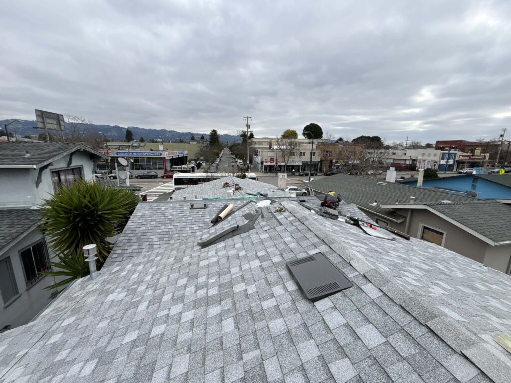 Roofing crew mid-repair on a shingle roof overlooking a San Jose commercial street
